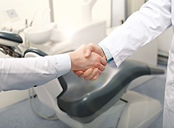 Close-up of patient shaking dentist’s hand in front of treatment chair