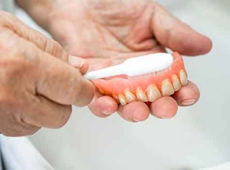 Set of dentures splashing into a clear glass full of transparent liquid