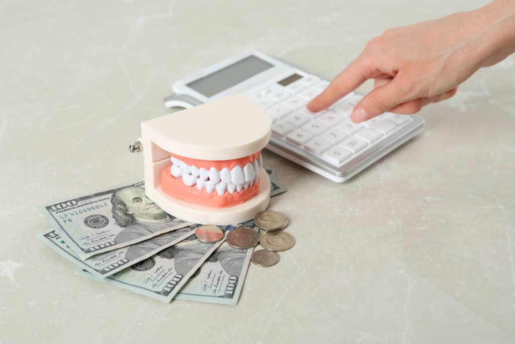 Model teeth on top of dollar bills next to a hand pushing calculator buttons